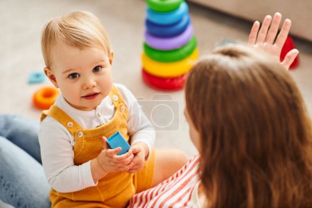 Photo for A baby girl and her mother interact, playing joyfully on the floor at home. - Royalty Free Image