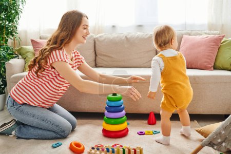 Foto de Una madre joven y su hija pequeña riendo y jugando en una acogedora sala de estar. - Imagen libre de derechos