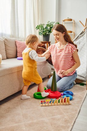 Une jeune mère joue joyeusement avec sa fille tout-petit dans un cadre confortable de salon, créant des souvenirs chéris ensemble.