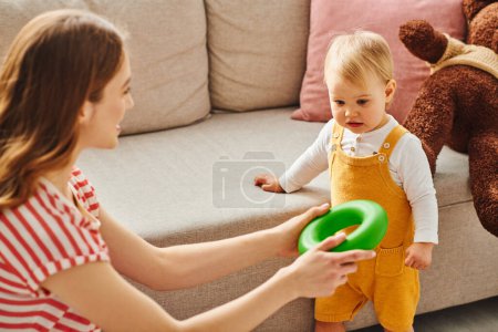 A young mother shares a playful exchange with her toddler on a cozy couch.