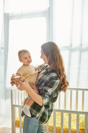 Photo for A young mother lovingly cradles her toddler daughter in her arms, sharing a sweet moment of connection and love at home. - Royalty Free Image