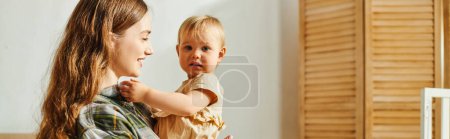 Photo for A young mother lovingly cradles her toddler daughter in her arms, exuding warmth and tenderness in their home. - Royalty Free Image