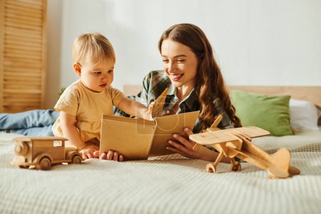 Une jeune mère lit un livre à sa petite fille, créant un moment magique d'amour et de connexion sur un lit confortable.
