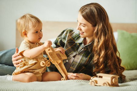 Téléchargez les photos : Une jeune mère interagit amoureusement avec sa fille tout-petit tout en jouant sur un lit confortable à la maison. - en image libre de droit