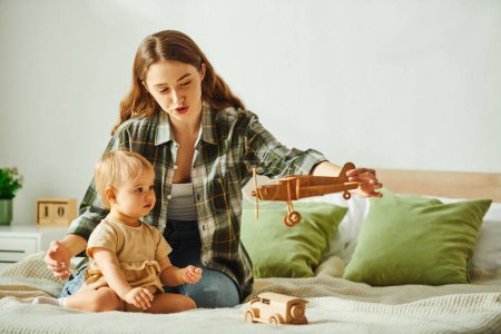 Photo for Young mother lovingly plays with her toddler daughter on a cozy bed, creating joyful and memorable family moments. - Royalty Free Image