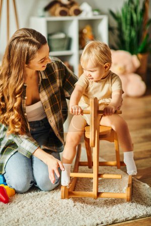 A young mother lovingly interacts with her baby daughter seated in a high chair, creating a heartwarming moment.