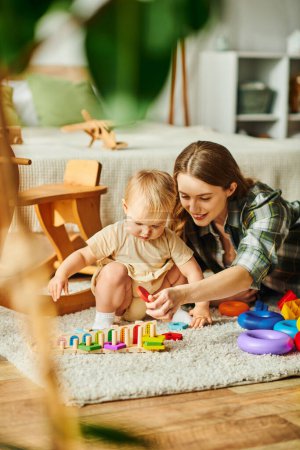 Téléchargez les photos : A young mother joyfully engages with her toddler daughter on the floor, fostering a strong bond through play and interaction. - en image libre de droit