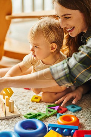 Foto de Una madre joven y su hija pequeña están jugando felizmente con juguetes en el suelo en casa. - Imagen libre de derechos