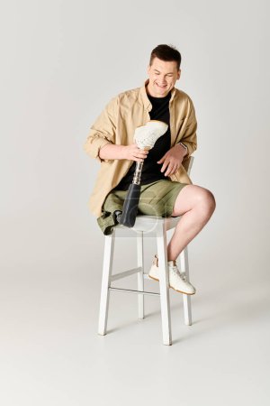 Handsome man in casual attire with prosthetic leg sitting on stool.