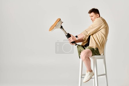 A handsome man with a prosthetic leg confidently sits atop a white stool.