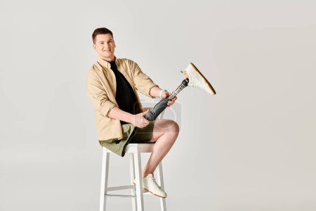 Téléchargez les photos : Bel homme avec une prothèse de jambe est assis avec confiance sur un tabouret. - en image libre de droit