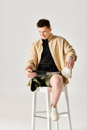 A handsome man with a prosthetic leg is actively posing while sitting on top of a white stool.
