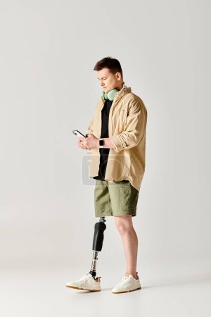 A handsome man with a prosthetic leg in a tan jacket uses a smartphone.