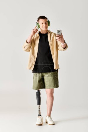 A man with a prosthetic leg wearing headphones and holding a cell phone.