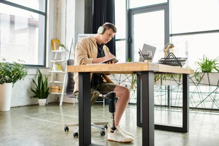 A handsome businessman with a prosthetic leg sits at a desk, focused on his laptop work.