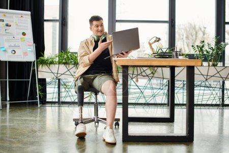A handsome businessman with a prosthetic leg sitting at a desk, focused on using a laptop.