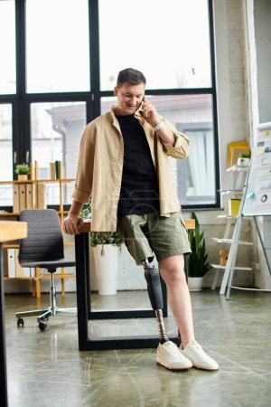 Foto de Un hombre de negocios guapo con una pierna protésica de pie en una oficina, entablando una conversación telefónica. - Imagen libre de derechos