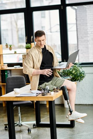 A handsome businessman with a prosthetic leg sits at a desk, working on a laptop computer.