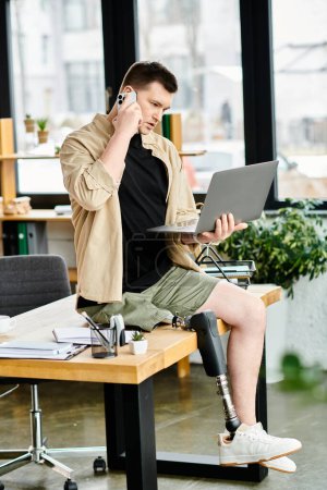 Un hombre de negocios con una pierna protésica se sienta en una mesa, usando un portátil y hablando por teléfono celular.