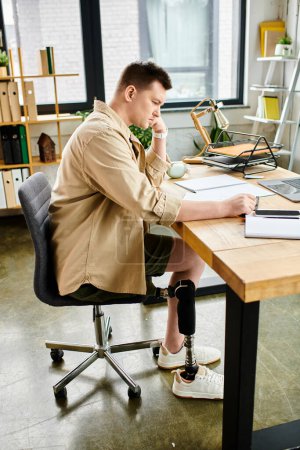 Photo for A handsome businessman with a prosthetic leg deep in work on a laptop at his desk. - Royalty Free Image