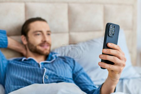 Man in bed at home holding a phone in hand, relaxing and unwinding.
