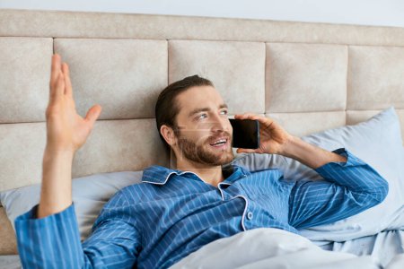 Téléchargez les photos : Un homme se couche paisiblement dans son lit, concentré sur son appel téléphonique. - en image libre de droit