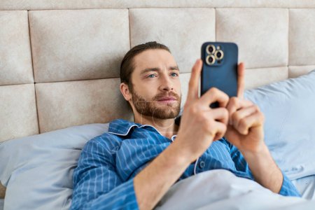 Serene man laying in bed, holding cell phone, enjoying a peaceful morning.