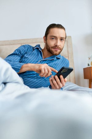 Ein Mann, der mit einem Handy beschäftigt ist, während er auf einem Bett sitzt, umgeben von ruhiger Energie.