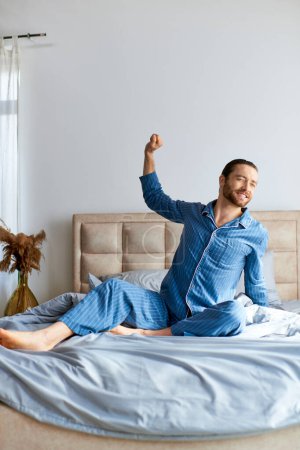 A man in pajamas sitting on a bed in a peaceful morning moment.