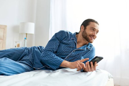 A man peacefully engaged with his cellphone while laying on a comfy bed.