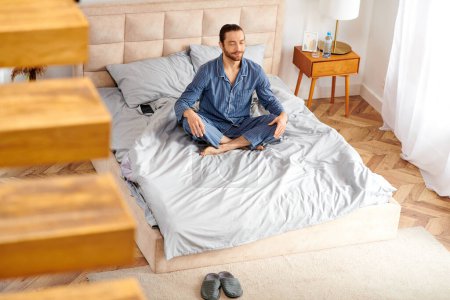 Téléchargez les photos : Beau homme pratique paisiblement le yoga du matin sur son lit. - en image libre de droit