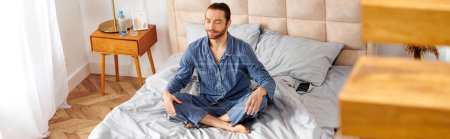 Schöner Mann praktiziert friedlich Yoga auf einem gemütlichen Schlafzimmerbett.