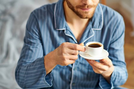 A handsome man in pajamas peacefully enjoying a cup of coffee.
