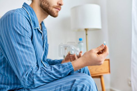 Téléchargez les photos : Un homme assis sur un lit, prenant la pilule dans une atmosphère chaleureuse le matin. - en image libre de droit