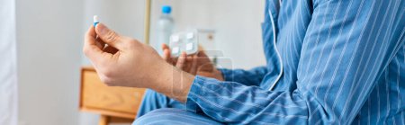 Foto de A man sits on a bed, holding a bottle of water and pill. - Imagen libre de derechos