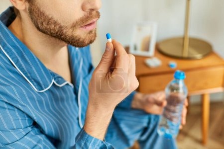 Photo for Handsome man in a blue shirt holding a bottle of water and pill. - Royalty Free Image