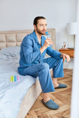 Handsome man resting on bed, hydrating with water in a serene morning setting.
