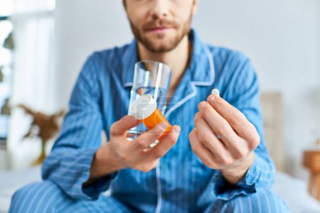 Téléchargez les photos : Un homme en pyjama tient sereinement un verre de liquide et prend des pilules. - en image libre de droit