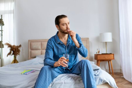 Photo for Man sitting on bed, drinking glass of water. - Royalty Free Image