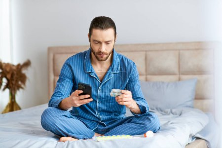 Photo for A man engrossed in his cell phone while sitting on a bed. - Royalty Free Image