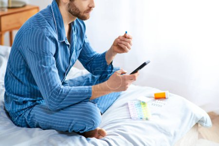 A man relaxes on a bed, holding pills and a cell phone.