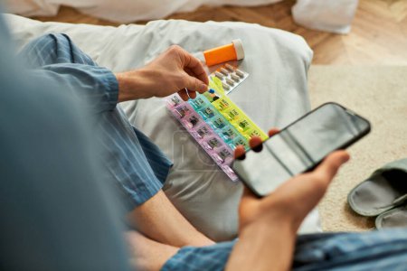 Téléchargez les photos : Un homme assis avec son téléphone et des pilules sur un canapé confortable. - en image libre de droit