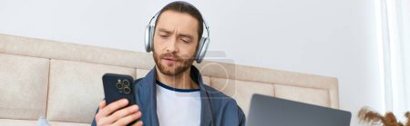 Photo for A man, headphones on, gazes at his cell phone screen. - Royalty Free Image