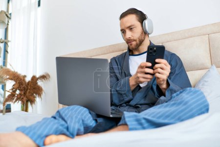 Téléchargez les photos : Un homme assis confortablement sur un lit, se concentrant sur son écran d'ordinateur portable. - en image libre de droit