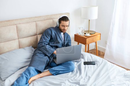A man relaxes on a bed, using a laptop in a peaceful morning setting.