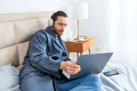 Man sitting on bed, focused on laptop screen.