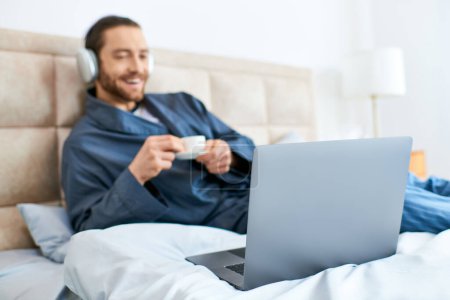 A man in bed engrossed in his laptop screen, creating a serene morning atmosphere.