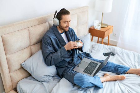 Foto de Un hombre inmerso en la tecnología en una cama con un ordenador portátil y auriculares. - Imagen libre de derechos