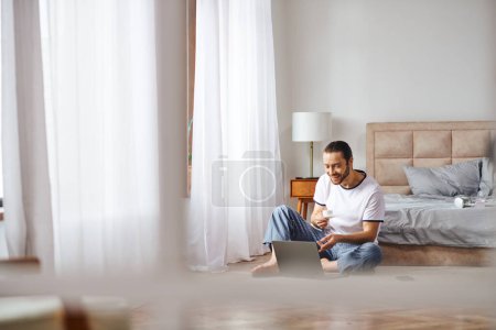 Ein Mann vertieft sich in Online-Aufgaben, während er auf dem Boden sitzt und Ruhe mit Technologie verbindet.