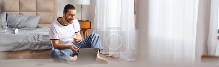 Téléchargez les photos : Un homme absorbé dans l'utilisation d'un ordinateur portable tout en étant assis sur le sol. - en image libre de droit